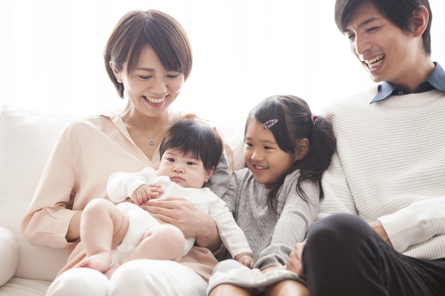 Parents, daughter and baby are sitting on the sofa and talking.